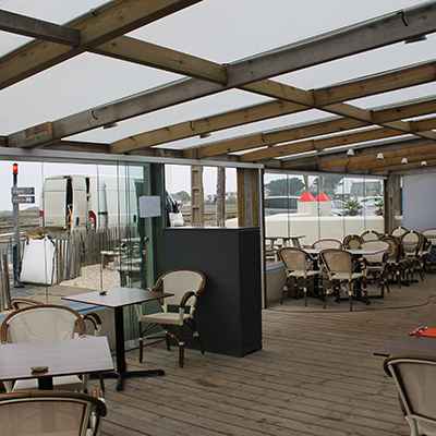 Installation d'un système de fermeture en verre qui ferme une grande terrasse couverte d'un restaurant de plage