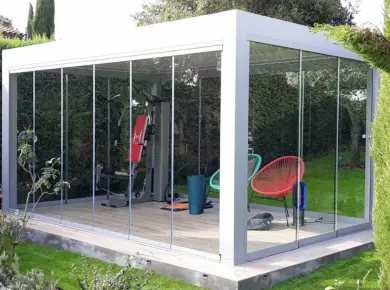 Pergola autoportante en aluminium fermée par des systèmes en verre pour créer une salle de sport au milieu du jardin