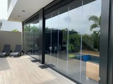 Rideau de verre sur mesure qui ferme une terrasse couverte d'un salon d'été avec profilé noir et porte de service