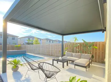 Pergola bioclimatique adossée au mur de la maison pour créer un toit de terrasse avec piscine attenante
